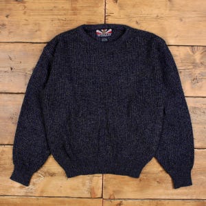 May include: A navy blue knitted sweater with a ribbed texture. The sweater features a crew neck and long sleeves. The brand name "BONKERS" is visible on the label. The sweater is made of a thick, warm material, suitable for cooler weather.