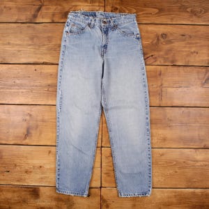 May include: Light blue denim jeans with a classic five-pocket design. The jeans have a straight leg cut and a faded wash, giving them a vintage look. The jeans are laid flat on a wooden surface.