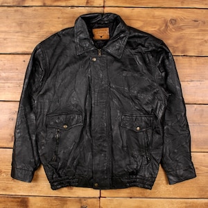 Könnte beinhalten: Schwarze Lederjacke mit Kragen, zwei Vordertaschen mit Knopfverschluss und zwei Reißverschlusstaschen. Die Jacke hat einen Reißverschluss und ein braunes Lederetikett mit der Aufschrift "Leather Works".