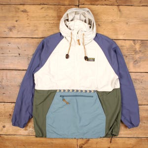 May include: A multi-colored anorak jacket with a hood. The jacket features a cream-colored front panel, blue sleeves, and a green and blue lower section. It has a front pocket and a small logo patch.