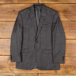 May include: A charcoal grey blazer featuring a subtle plaid pattern, a notched lapel, two front buttons, a chest pocket, and two flap pockets. The sleeves are finished with four small buttons at each cuff, and the interior is lined.
