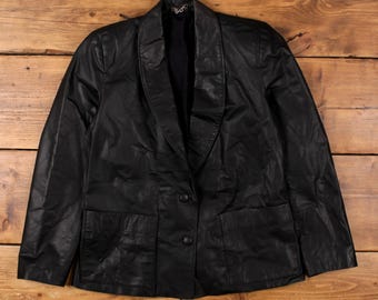 May include: A black leather blazer with a notched lapel, two front pockets, and two-button closure. The jacket is displayed on a wooden surface. The blazer has a classic, tailored design.