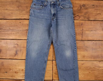 Puede incluir: Un par de pantalones vaqueros de mezclilla en tono azul medio con un diseño clásico de cinco bolsillos, cierre de botón y cremallera, trabillas para cinturón y un corte relajado. Los vaqueros tienen un aspecto desgastado en los muslos.