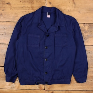 Puede incluir: Chaqueta de trabajo azul marino con cierre de botones, dos bolsillos en el pecho y cuello. La chaqueta tiene botones negros y una pequeña etiqueta en el cuello. La chaqueta está hecha de tela duradera.