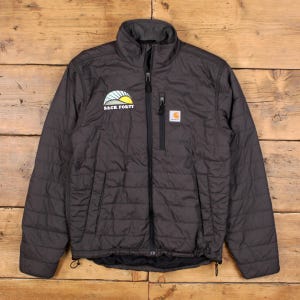 May include: Dark gray quilted jacket with a full-length zipper and a stand-up collar. The jacket features a "Back Forty" logo on the left chest and a Carhartt logo on the right chest. The jacket has two zippered pockets and a drawstring at the bottom.