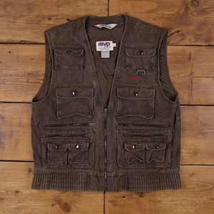 Op de afbeelding: Een bruin utility-vest met meerdere zakken met drukknopen en horizontale ritsvakken. Het kledingstuk is voorzien van een centrale ritssluiting, een geribbelde zoom en een wit label in de nek aan de binnenzijde met de tekst MVP en Jim Beam.