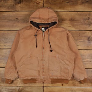 May include: A brown hooded jacket with a zipper closure, two front pockets, and a ribbed hem and cuffs. The jacket has a drawstring around the hood and a dark brown lining. The jacket is made of a durable, workwear-style material.
