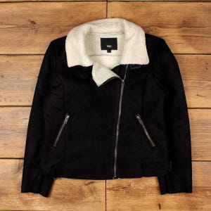 May include: A black jacket with a white faux shearling collar and lining. The jacket features an asymmetrical front zipper closure, two zippered pockets on the front, and a black label with white text inside the collar area.