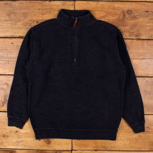 May include: A solid dark navy blue quarter-zip pullover sweater featuring a high collar, long sleeves with ribbed cuffs, and a matching ribbed hem. The garment includes a central zipper closure with a small brown leather pull tab at the top.