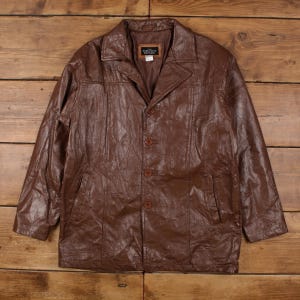 May include: Brown leather jacket with a collared neckline and button closure. The jacket has two front pockets and a textured surface. The tag inside the jacket reads "Executive".