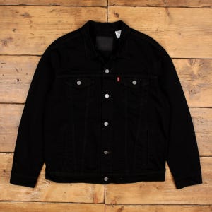May include: A black denim jacket featuring a classic collar, long sleeves, and a button-down front closure. The jacket includes two chest pockets with buttoned flaps, silver-toned metal buttons, and a small red brand tab on the left pocket.
