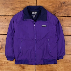 Puede incluir: Chaqueta morada Lands' End con cuello y ribetes azul marino. La chaqueta tiene cremallera completa, dos bolsillos delanteros y el logotipo de Lands' End en el pecho. La chaqueta está hecha de un material liso y resistente al agua.
