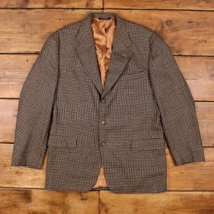Può includere: Un blazer con motivo pied-de-poule marrone e nero, caratterizzato da revers dentellati, tre bottoni frontali e due tasche con patta. L'interno è foderato in tessuto beige a tinta unita, con maniche lunghe e una struttura definita sulle spalle.