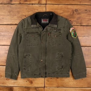 May include: Olive green Levi's jacket with a black collar and a patch on the right sleeve. The jacket has two chest pockets and two lower pockets. The Levi's logo is visible on the inside of the collar. The jacket is buttoned up and has a classic, rugged style.
