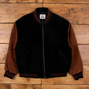 May include: Black bomber jacket with brown suede sleeves. The jacket has a zip-up front, a ribbed collar, cuffs, and hem with brown stripes. The label on the collar reads "BASIC EDITIONS".