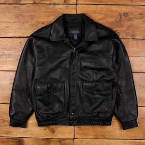 Puede incluir: Chaqueta de cuero negra con cremallera, dos bolsillos delanteros y cuello. La chaqueta tiene dobladillo y puños acanalados. La marca "Editions" es visible en una etiqueta dentro del cuello.