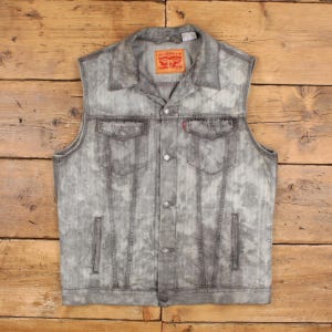 Può includere: Un gilet in denim grigio con effetto lavaggio acido, colletto classico, chiusura frontale con bottoni, due tasche sul petto con patta abbottonata e due tasche laterali verticali. Un'etichetta rossa Levi's è cucita sul collo e sulla tasca.