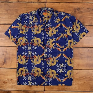 Puede incluir: Una camisa azul de manga corta con un patrón repetido de dragones dorados, detalles rojos y diseños florales y de escritura blancos. La camisa tiene un cuello clásico, un bolsillo en el pecho y el nombre de la marca "ALPES" visible en el cuello.