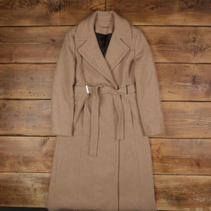 May include: A tan Calvin Klein long coat with a belted waist and a notched collar. The coat has a double-breasted design and a black interior lining. The coat is made of a soft material and has a classic, elegant style.