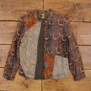 Könnte beinhalten: Eine Patchwork-Jacke mit verschiedenen Paisley- und Blumenmustern in Braun-, Orange- und Grautönen. Die Jacke hat einen durchgehenden Reißverschluss und einen Kragen. Der Stoff scheint eine Mischung aus Texturen zu sein, darunter ein tweedartiges Material.
