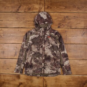 May include: A camouflage hooded jacket in shades of brown, tan, and gray. The jacket features a full zipper, a hood, and reinforced panels on the shoulders and sleeves. The jacket has a small red logo on the chest.