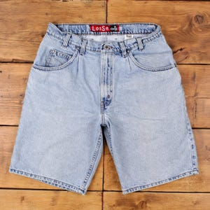 May include: Light blue denim shorts with a classic five-pocket design. The shorts have a button and zipper closure, belt loops, and the word "Loose" on the waistband. The shorts are made of a light wash denim.