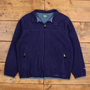 Puede incluir: Chaqueta polar azul marino con cierre de cremallera completo, dos bolsillos laterales y cuello y ribetes azul claro. La chaqueta presenta el logotipo "L.L.Bean" en la parte inferior derecha y un pequeño logotipo en el pecho izquierdo.