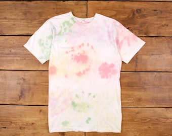 May include: A white tie-dye t-shirt with pink, yellow, and green swirls. The shirt is made of a soft, comfortable material and has a relaxed fit.