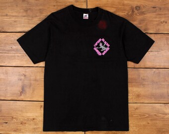 May include: Black t-shirt with a pink graphic of a figure in a diamond shape with the text "Captain Black Shred Wear".