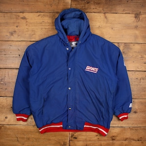 May include: A blue hooded jacket with the word "GIANTS" in white and red lettering. The jacket has a red and white striped trim on the cuffs and hem. The jacket has a snap closure and a Starter logo.