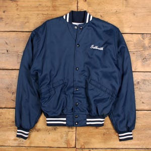 May include: A navy blue bomber jacket with white striped detailing on the cuffs and collar. The jacket features a button-up front and two front pockets. The name "Galbraith" is embroidered in white script. Made from a shiny material, possibly nylon.