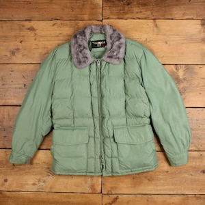May include: A sage green quilted puffer jacket featuring a grey faux fur collar, a full-length front zipper closure, and two large rectangular patch pockets at the waist. The interior label displays the brand name Temper in white text.