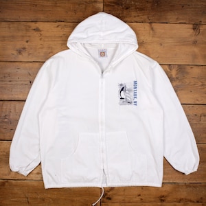 Puede incluir: Chaqueta blanca con capucha y cremallera con un gráfico de velero y el texto "MONTAUK, NY". La chaqueta tiene un cordón en la parte inferior y dos bolsillos delanteros. El gráfico es azul y blanco.