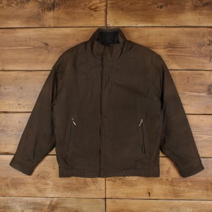May include: A dark brown jacket featuring a high collar, a central front zip concealed by a placket, and two side pockets with silver-toned zips. The jacket has long sleeves with cuffs and a straight hemline, presenting a solid colour design.