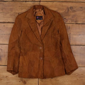 May include: A brown suede blazer with a patchwork design. The jacket features a notched collar, two-button closure, and a tailored fit. The blazer is made of a soft, textured material and is suitable for various occasions.