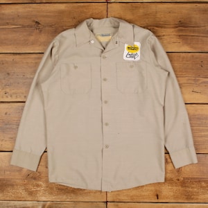 May include: A tan long-sleeve work shirt with two chest pockets and a button-down front. The shirt has a collar and a patch on the right chest that reads "midas" and "Goodyear Shoes".