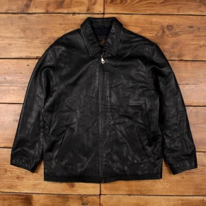 May include: A black leather jacket with a collared neckline and a full-length zip. The jacket has two front pockets and a classic design. The leather has a slightly distressed appearance, giving it a vintage look. A timeless piece.