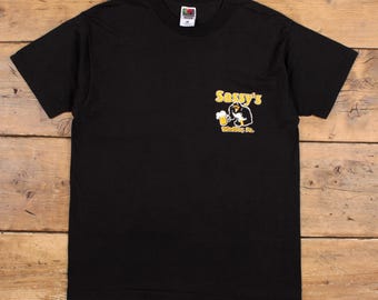 May include: Black t-shirt with a small graphic on the front. The graphic features a cartoon character holding a beer mug, with the text "Sassy's" above and "Winding Pa." below. The shirt is made of a soft material.