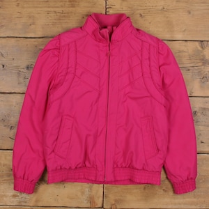 May include: A vibrant fuchsia jacket with a full zipper closure. The jacket features a stand-up collar, elasticized cuffs, and a ribbed hem. The design includes stitched chevron details on the front and shoulder panels, and two front pockets. A retro style jacket.