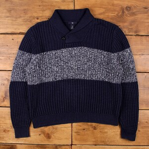 Könnte beinhalten: Ein marineblauer Pullover mit strukturiertem Waffelstrickmuster. Der Pullover hat einen grau-weiß gesprenkelten horizontalen Streifen über der Brust. Er hat einen Schalkragen und einen einzelnen Knopfverschluss. Das Gap-Logo ist auf dem Kragen sichtbar.