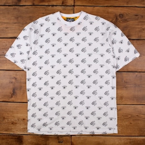 May include: White t-shirt with a repeating pattern of black "SP" initials and crowns. The shirt has a yellow collar and short sleeves. The shirt is made of a soft material.