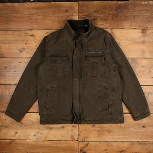May include: A dark olive green utility jacket featuring a stand-up collar, a full-length front zip with a snap-button placket, two chest pockets with flaps, and two lower vertical slit pockets. The jacket has long sleeves and a structured design.