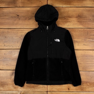 Könnte beinhalten: Schwarze Fleecejacke mit Kapuze und durchgehendem Reißverschluss. Die Jacke hat ein kleines weißes Logo auf der Brust und zwei Vordertaschen. Hergestellt aus einem weichen, warmen Material, ideal für Outdoor-Aktivitäten.