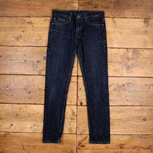 Könnte beinhalten: Dunkelblaue Jeans aus Denim mit Knopfleiste und klassischem Fünf-Taschen-Design. Die Jeans haben einen geraden Bein-Stil mit einem leicht verblichenen Aussehen. Das Kleidungsstück liegt flach auf einer Holzoberfläche.