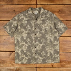 May include: A short-sleeved button-down shirt with a tropical leaf pattern in shades of gray and beige. The shirt has a classic collar and brown buttons. The L.L.Bean brand label is visible at the top.