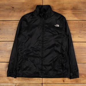 Könnte beinhalten: Schwarze Jacke mit durchgehendem Reißverschluss und Stehkragen. Die Jacke hat ein weißes Logo auf der Brust und zwei Seitentaschen. Die Marke The North Face ist sichtbar. Die Jacke besteht aus leichtem, möglicherweise wasserabweisendem Material.