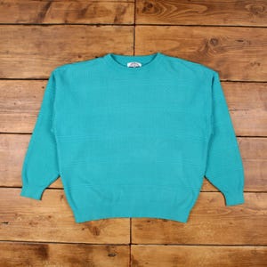 Könnte beinhalten: Ein türkisfarbener Rundhals-Pullover mit horizontalen strukturierten Streifen. Der langärmlige Pullover ist aus einem Strickstoff gefertigt. Der Pullover liegt flach auf einer Holzoberfläche.