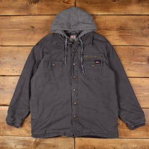 May include: A charcoal gray long-sleeve jacket featuring a detachable heather gray jersey hood with drawstrings, a button-down front closure, two chest pockets with button flaps, and a small zippered pocket above the left chest pocket with a Dickies logo.