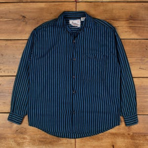 May include: A long-sleeve button-down shirt featuring a vertical striped pattern in alternating shades of dark blue and black. The shirt includes a standard collar, a single chest pocket on the left side, and dark buttons running down the front placket.