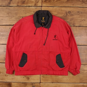 May include: Red jacket with a black collar and two front pockets. The jacket has a zipper closure and the Browning logo on the chest and collar. The jacket is made of a lightweight material.